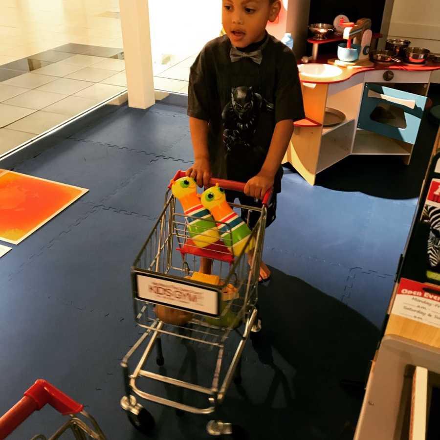 Young autistic boy pushes toy shopping cart with toys in it