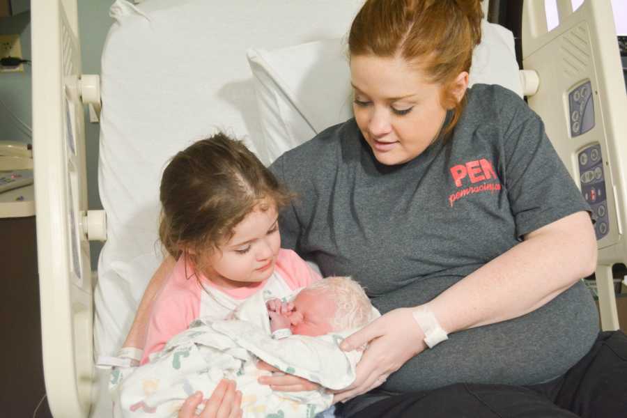 Mother who just gave birth to albino newborn with white hair sits beside first born holding new sibling