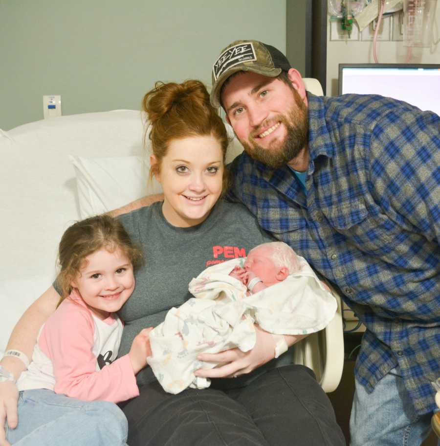 Mother who just gave birth sits with albino newborn in lap with first born and husband on either side of her