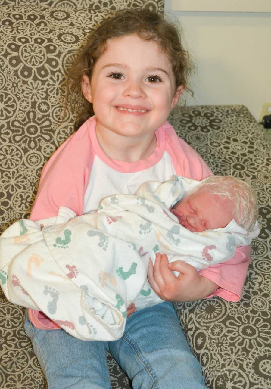 First born smiles as she holds albino new born sibling with white hair in her arms