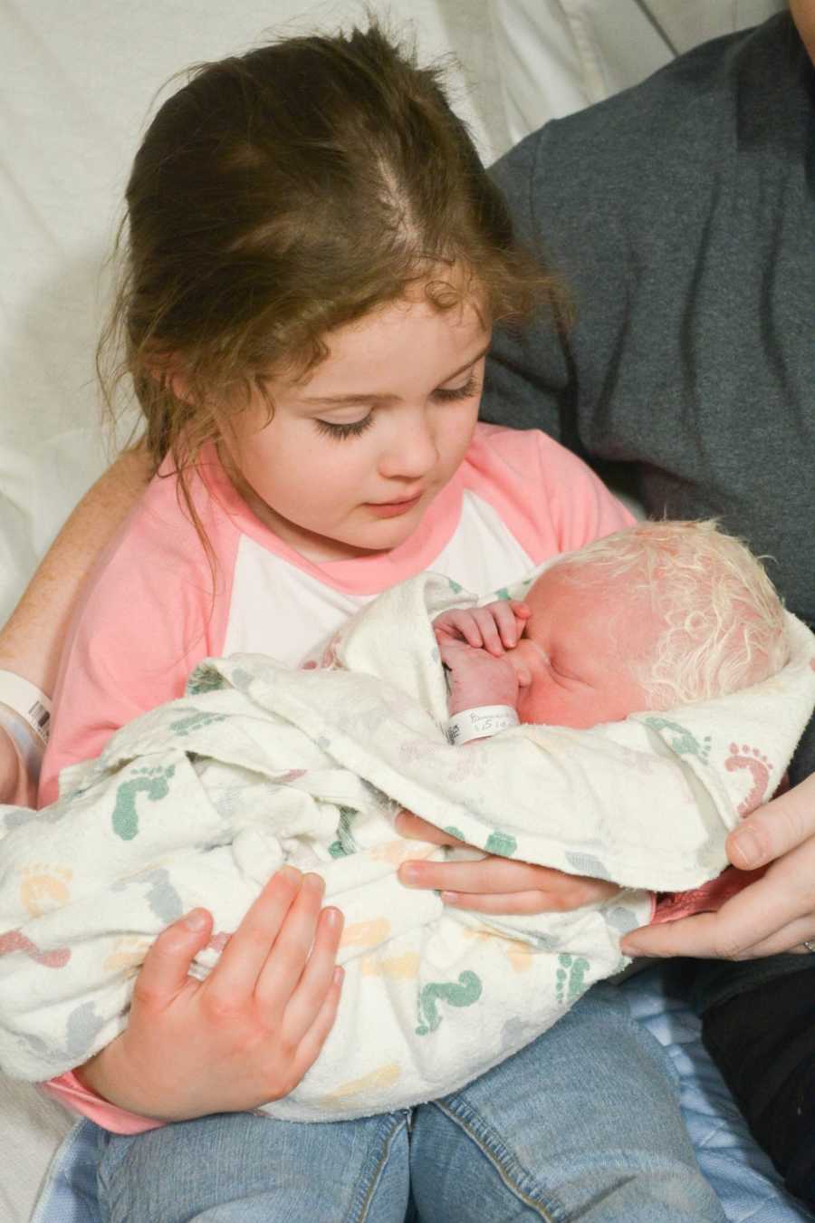 First born holds albino newborn sibling with white hair in her arm