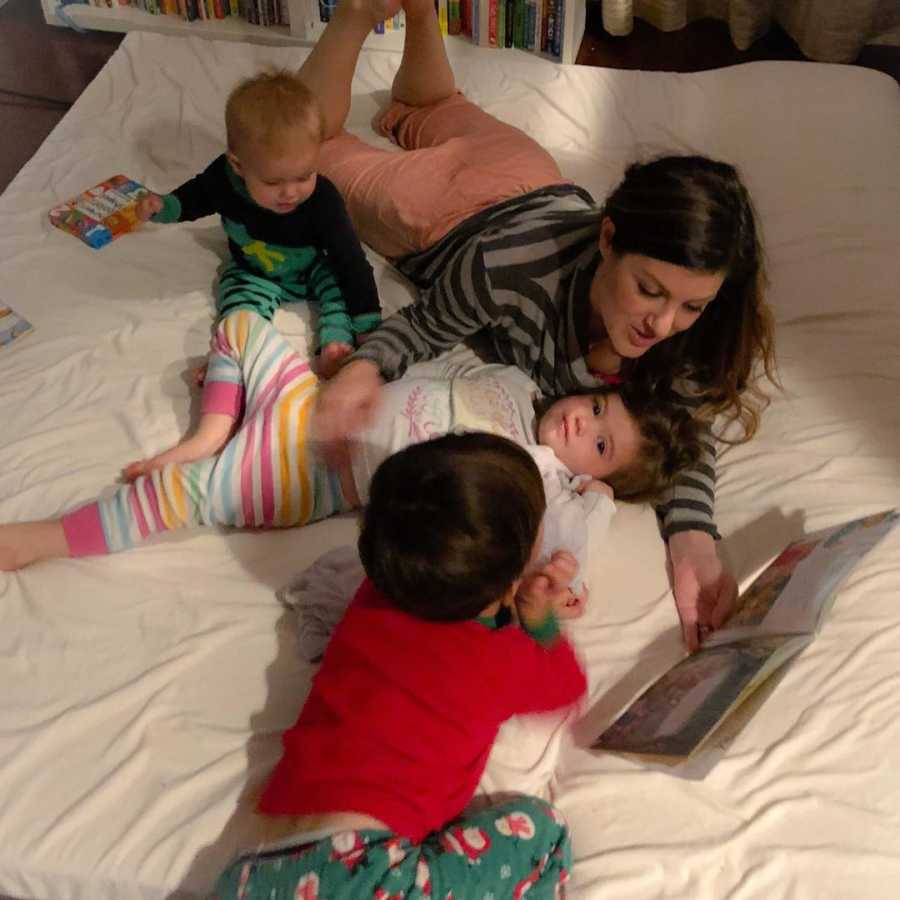 Woman who can't sleep at night due to children lays in bed reading book to three toddlers