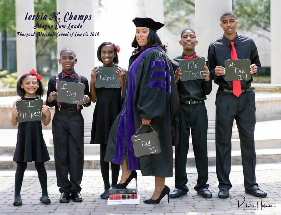 Single mother of five stand in cap and gown in front of children after graduating law school