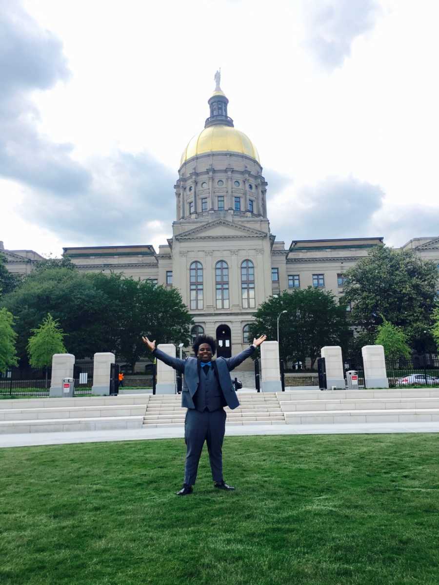 Teen stands in front state building with arms in air dressed for girlfriend's prom