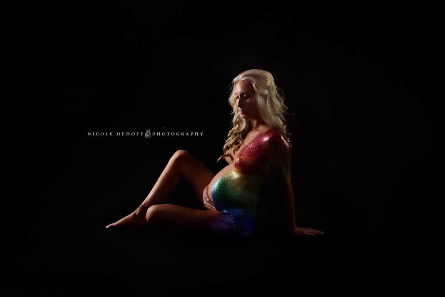 Pregnant woman sits holding her stomach with rainbow sparkles along side of her body