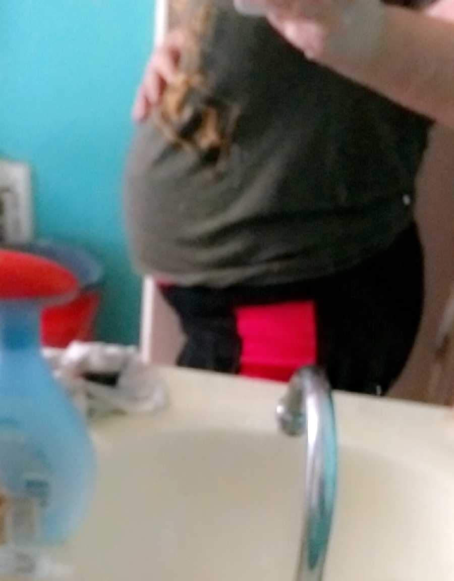 Blurry mirror selfie of pregnant woman holding her stomach