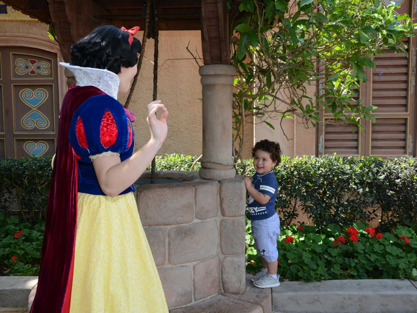 Toddler stands behind pillar peeking out at Snow White at Disney World