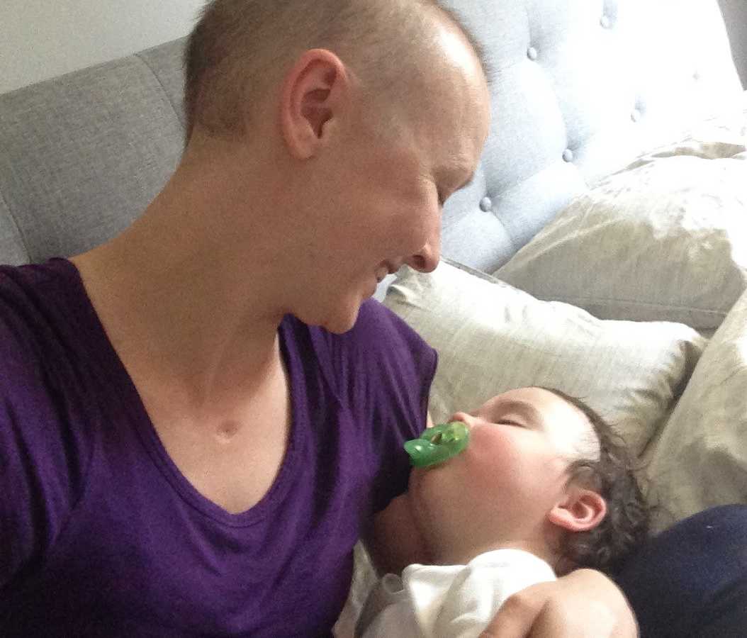 Woman with cancer smiles down at toddler sleeping in her lap