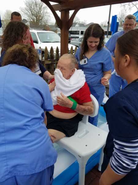 Elderly man drying off after he was baptized in inflatable pool with rehab nurses surrounding him