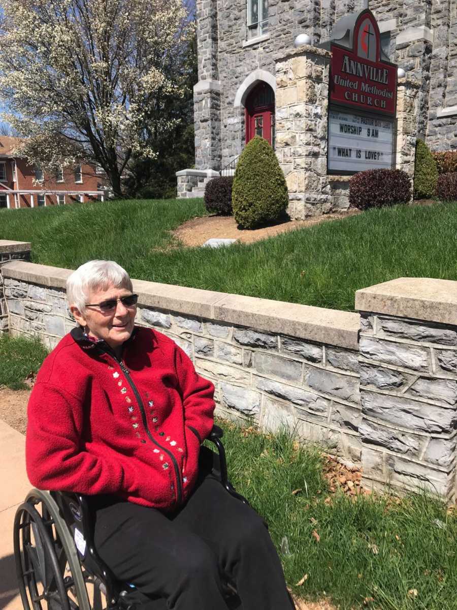 Woman with dementia sitting and smiling in wheelchair beside church