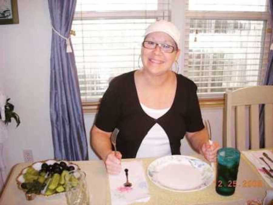 Motherless woman sits at set table smiling 