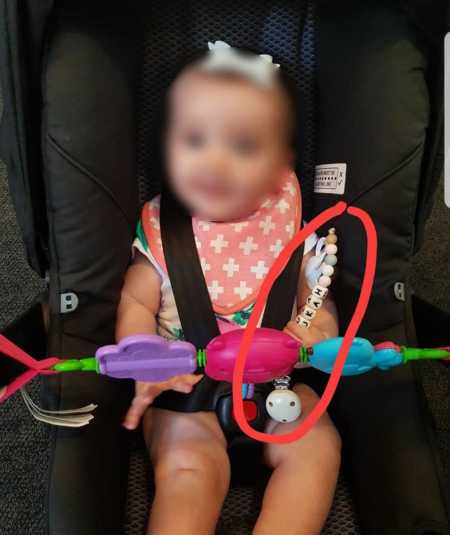 Baby in car seat with face blurred out holding teething toy that caused her to choke