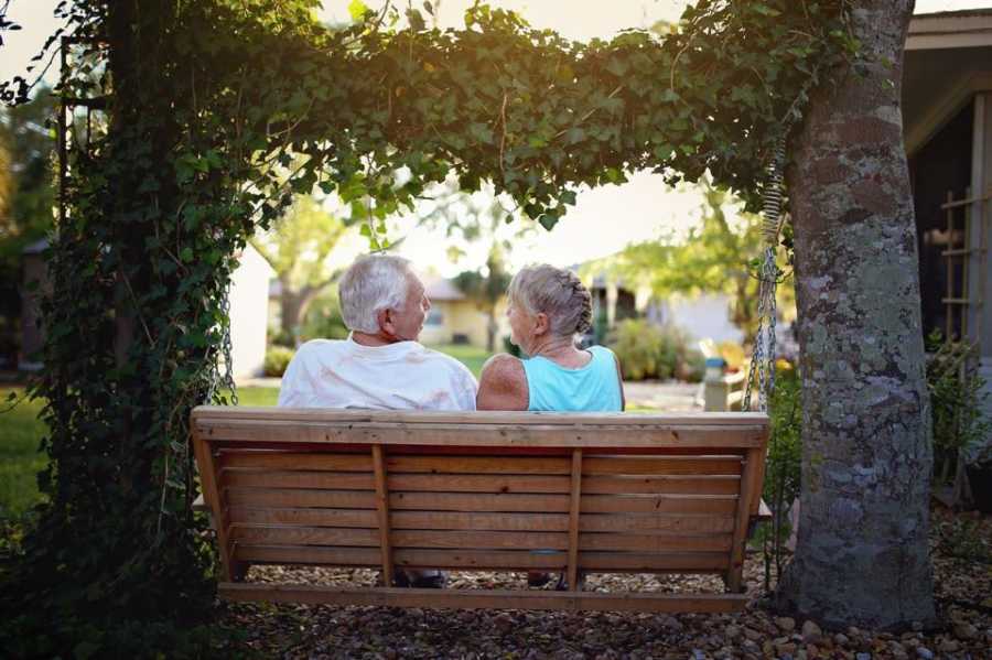 Husband and wife who helped raise their granddaughter sits on bench under tree