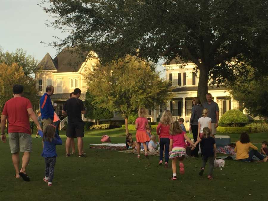 Play group of two year olds sitting on grass with parents standing nearby 