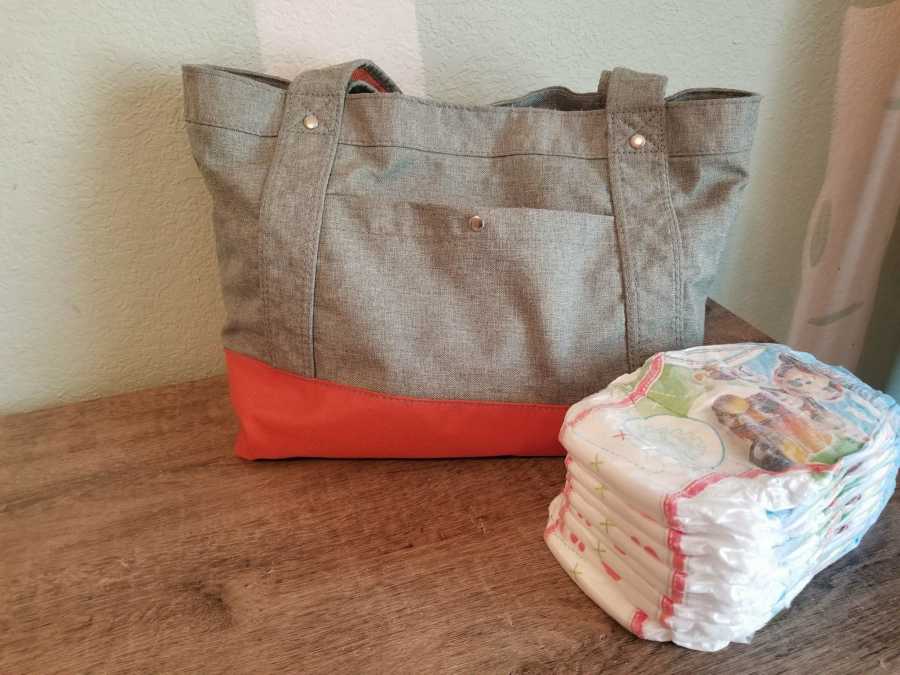 Diaper bag sitting on wooden table next to stack of diapers