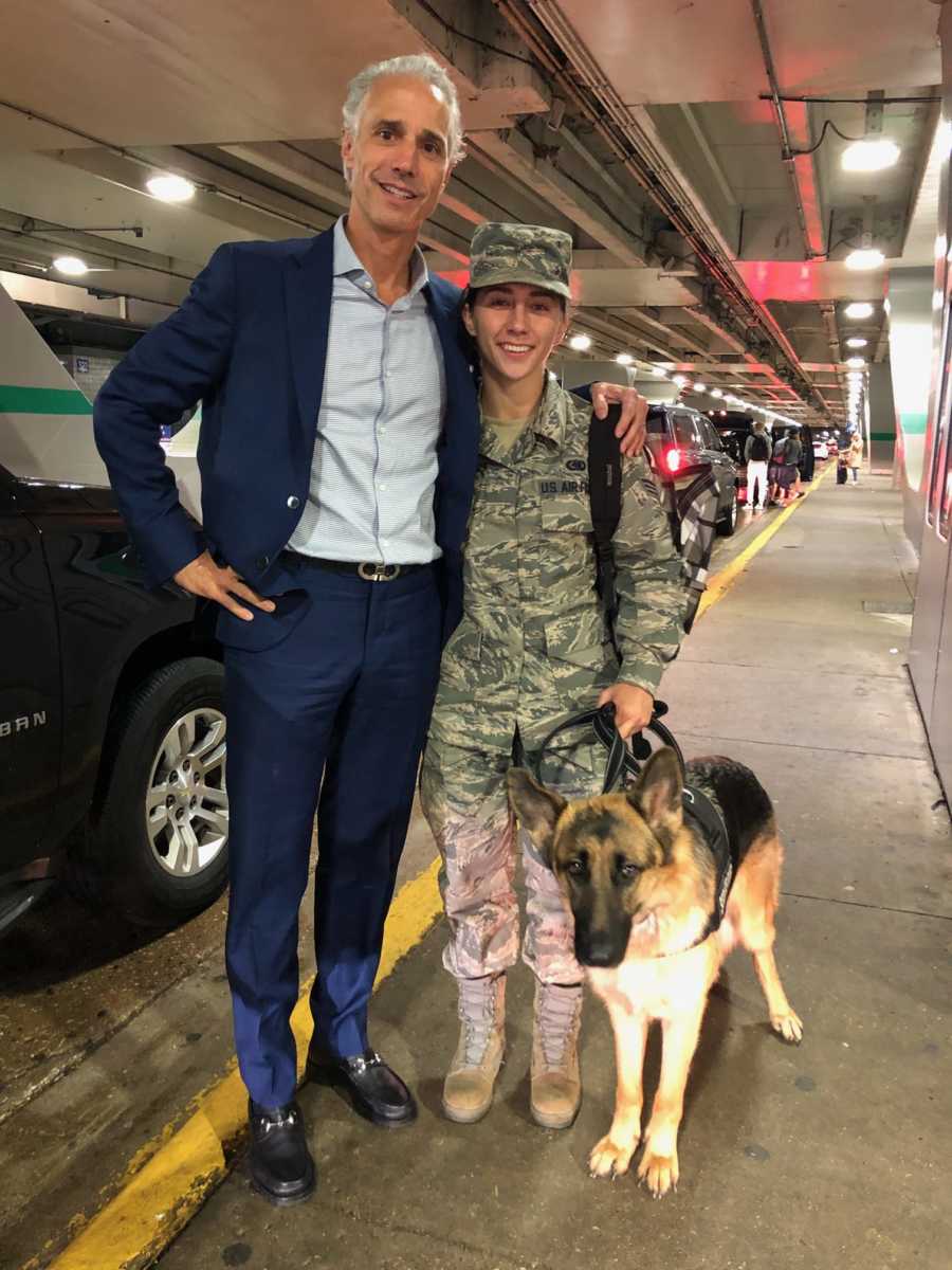 Stranger who bought airman ticket to see dying father stands with arm around her at airport