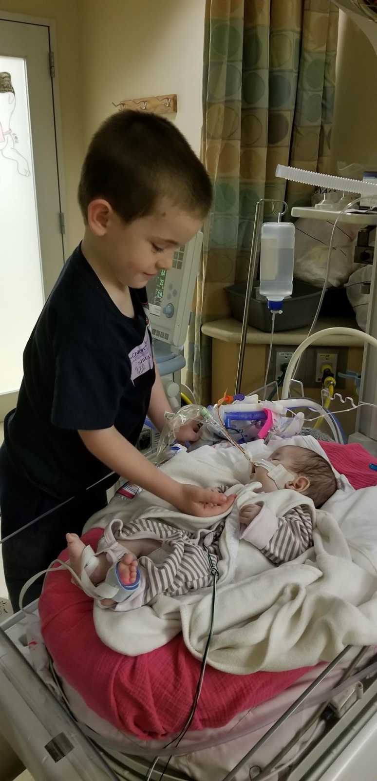 Toddler brother stands over baby sister in NICU