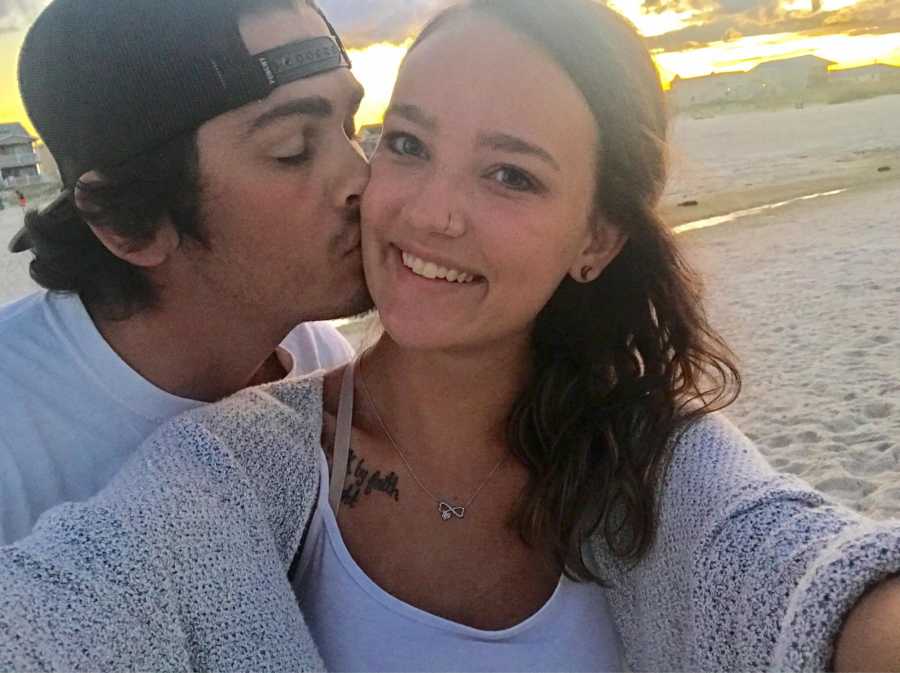 Girlfriend smiles in selfie while boyfriend kisses her on cheek