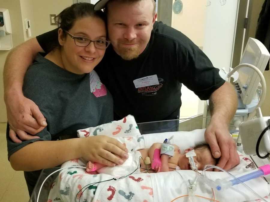 Mother and father smile while standing over newborn in NICU