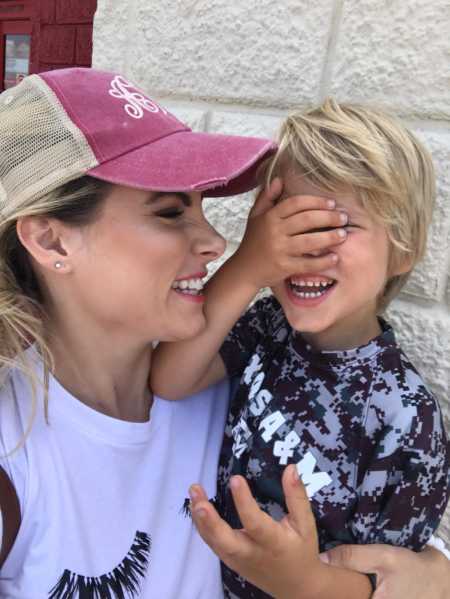 Mother smiling at son in her arms who is smiling holding hand over his face