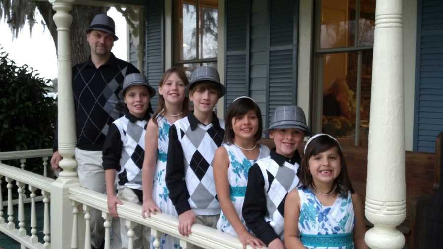Father standing behind six adopted children on front porch in matching outfits