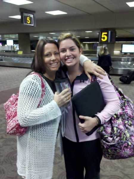 Birth mother stands with daughter who was adopted at birth at airport baggage claim