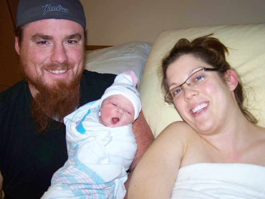 Father holding newborn next to wife in hospital bed after giving birth
