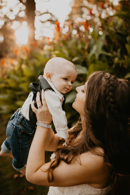 Bride smiles at son while holding him in the air