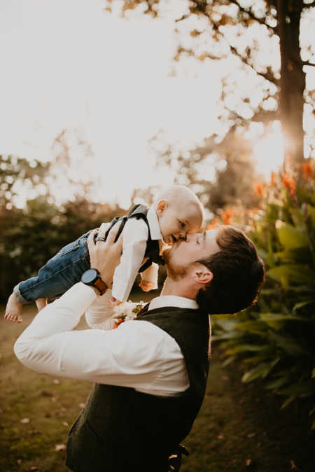 Husband holds baby son in the air kissing him