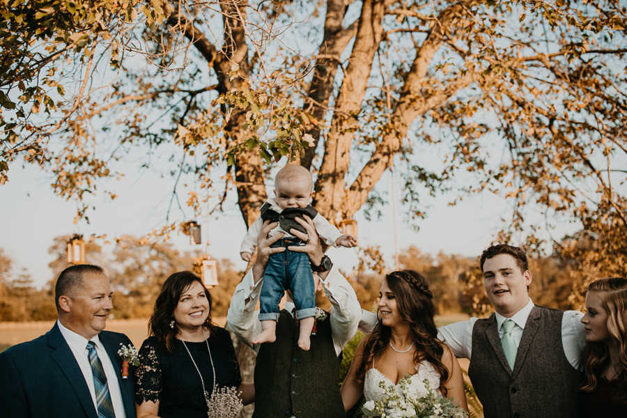 Groom holding baby son in air besides wife and family