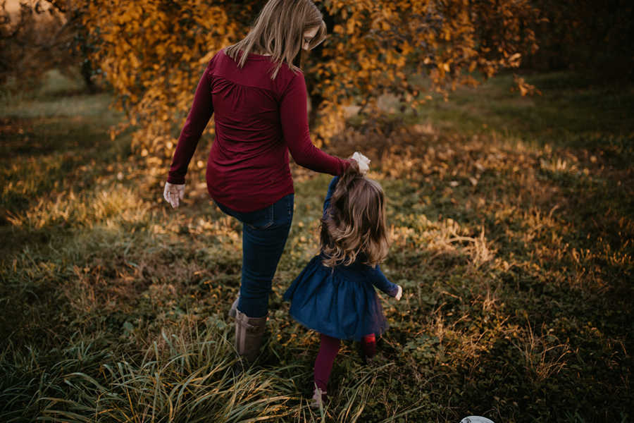 Mother with breast cancer holds young daughter's hand as they walk in grassy field