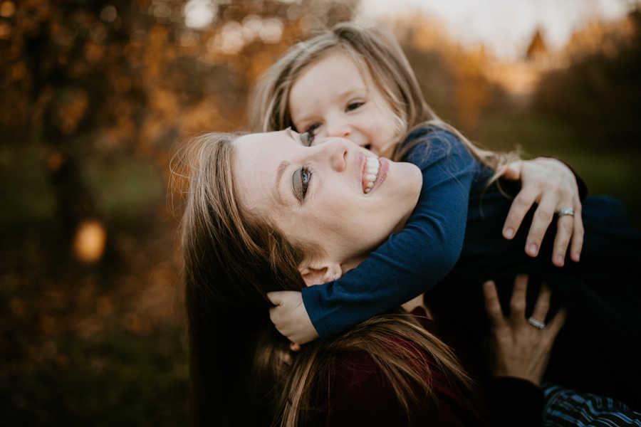 Mother with breast cancer smiles while holding toddler daughter in air