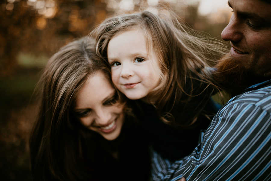 Toddler daughter smiles while father and mother with breast cancer holds her