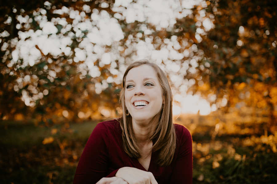 Mother with breast cancer smiles with trees and sunset behind her