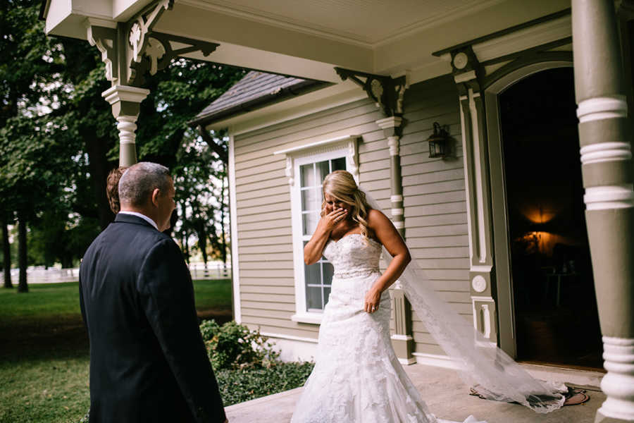 Bride crying as she walks out of front door of house towards her dad