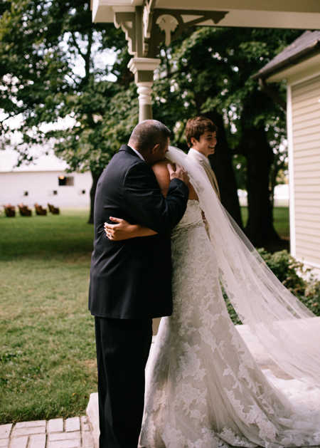 Father hugs his daughter in wedding dress while brother walks away smiling