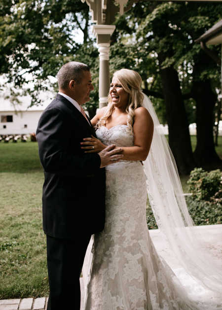 Bride holds on to father as she smiles while looking at him