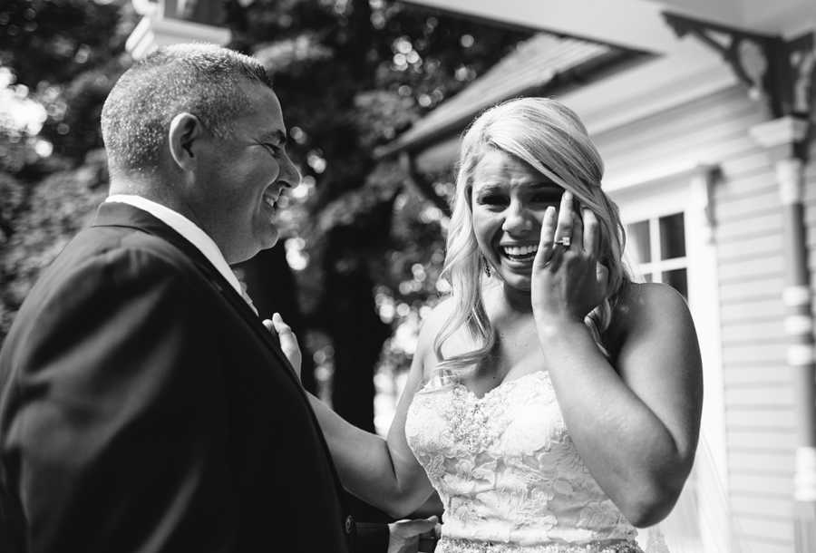 Bride smiles while wiping away tear while her father smiles