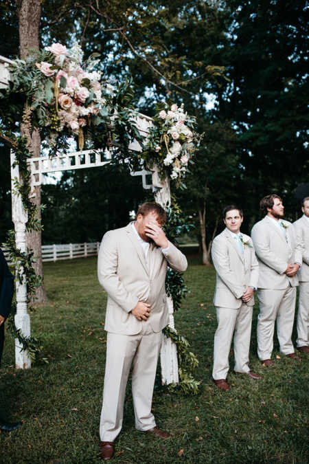 Groom holds his hand to his face while crying at altar of outdoor wedding