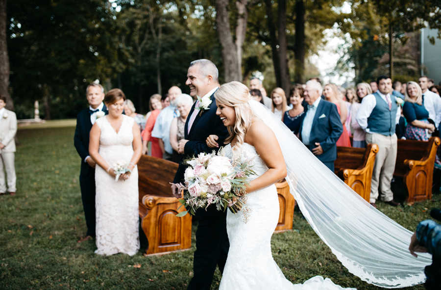 Father and daughter walk down the aisle smiling at outdoor wedding in yard