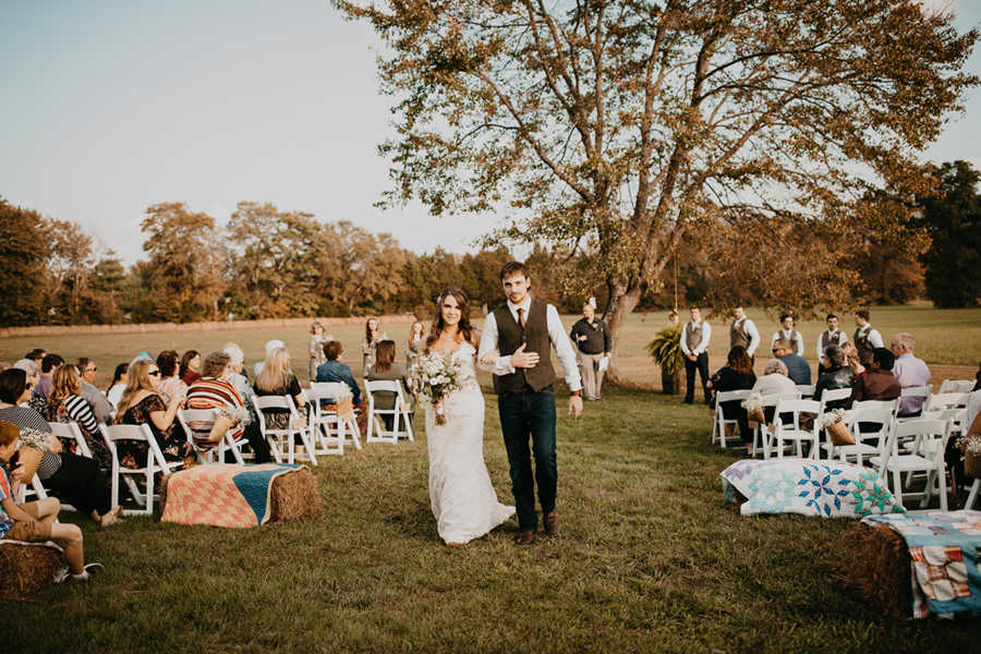 Bride and groom are arm in arm walking down the aisle of outdoor wedding