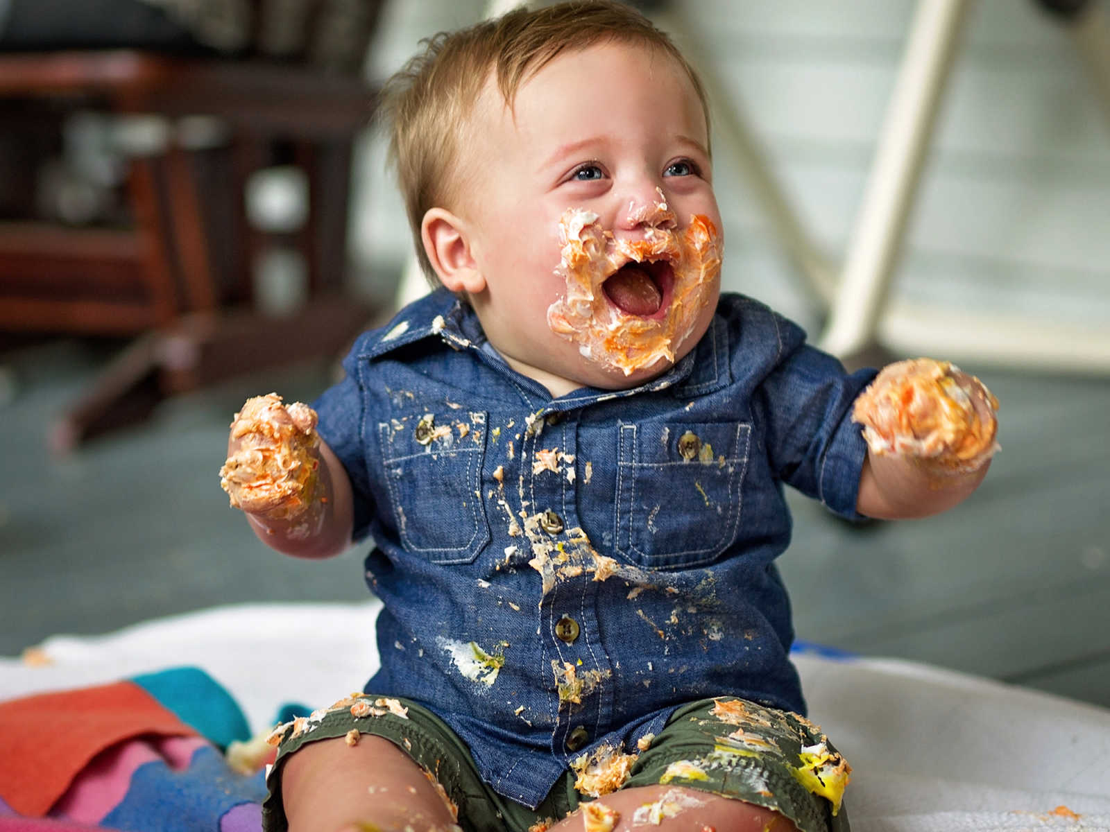 Toddler boy smiles while sitting on ground with cake and frosting all over him