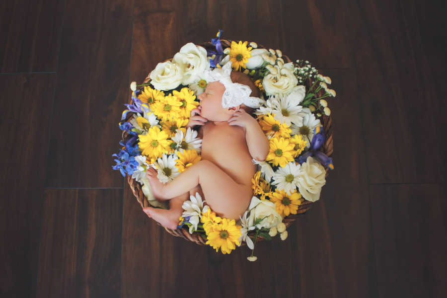 Newborn of two women laying in basket of flowers