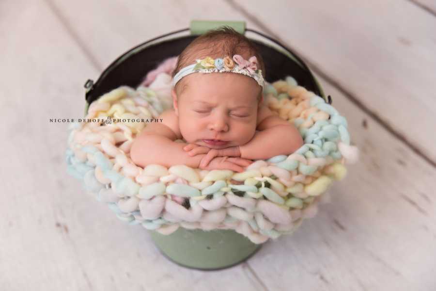 Newborn of woman who struggled with miscarriages sits in bucket with rainbow knit blanket