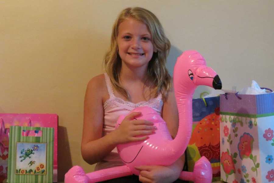 Young girl who struggles with extreme headaches smiling and holding inflatable flamingo