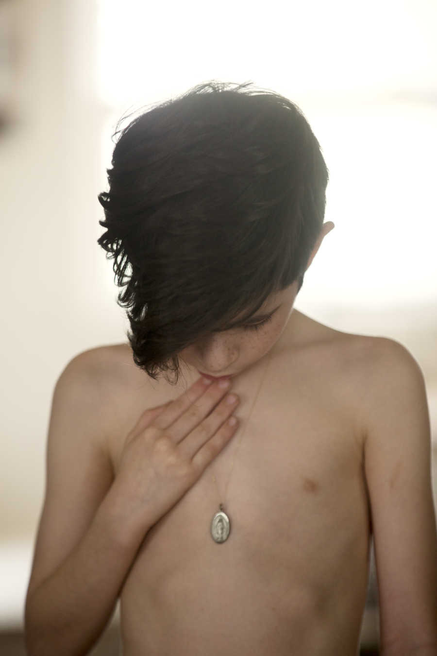 Boy whose father passed away looks down at angel necklace around his neck