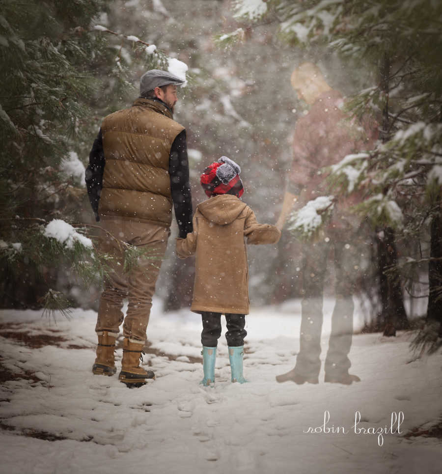 Young boy holds hands with mother's boyfriend in snowy forest while looking to side seeing ghost of dad