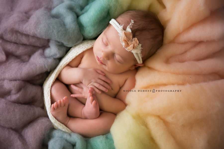 Newborn of mother who suffered from miscarriages sits in rainbow blanker