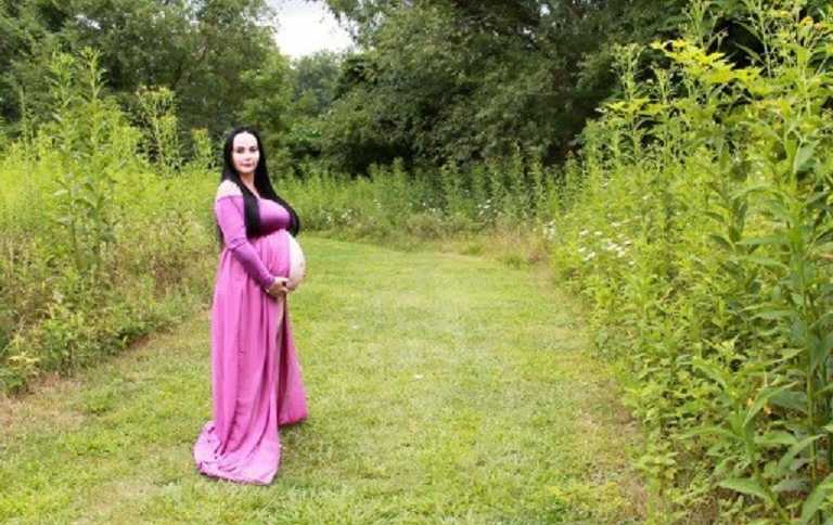 Pregnant woman through sperm donor holding her stomach in field in long pink dress