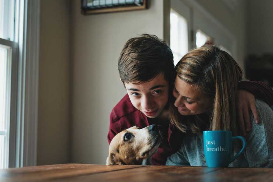 Boy who was adopted by his teacher has his arm around her and dog is close by